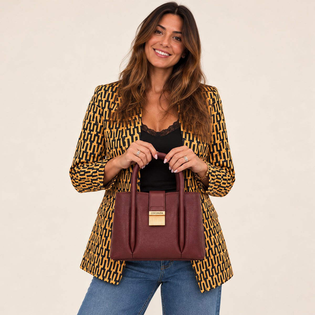 City Bag Coconuda Borgogna tenuta con entrambe le mani, abbinata a un blazer fantasia